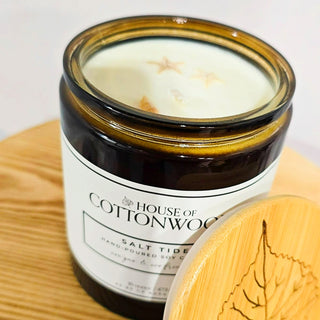 Candle in a glass jar labeled 'House of Cottonwood' on a bamboo surface.