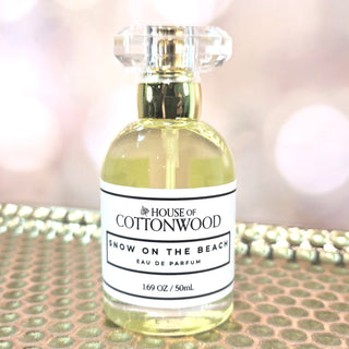 Perfume bottle labeled 'House of Cottonwood Snow on the Beach' on a reflective surface.
